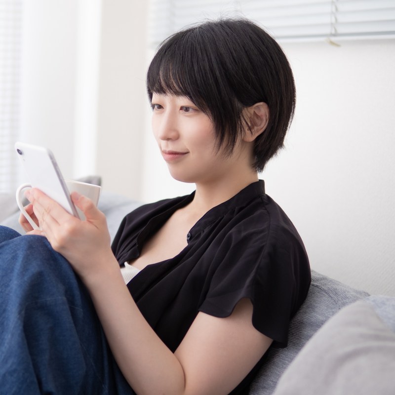 自宅のソファでスマートフォンを見ながら過ごす女性